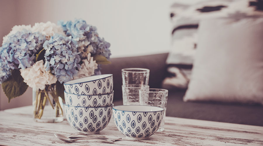 Three blue and white patterned bowls stacked on a table next to a vase of flowers and glasses.