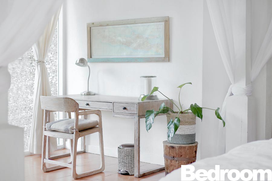 A wooden desk with a chair and a map framed on the wall in a bedroom setting.