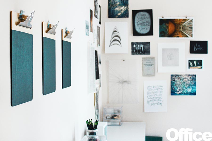 Three clipboards mounted on a wall with various framed artworks and prints surrounding them.