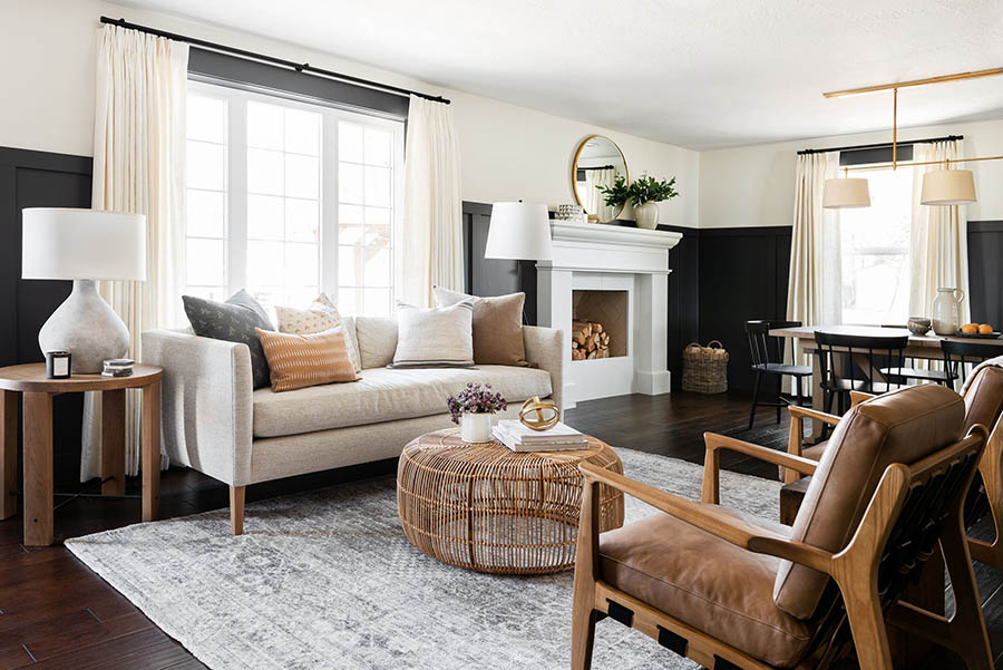 A modern living room featuring a beige sofa, wooden chairs, and a round coffee table on a patterned rug.
