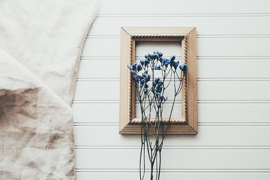 A gold-framed picture with dried blue flowers placed inside on a light background.