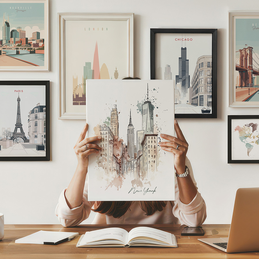 Individual holding a New York City art print while seated at a desk with various framed city prints in the background.