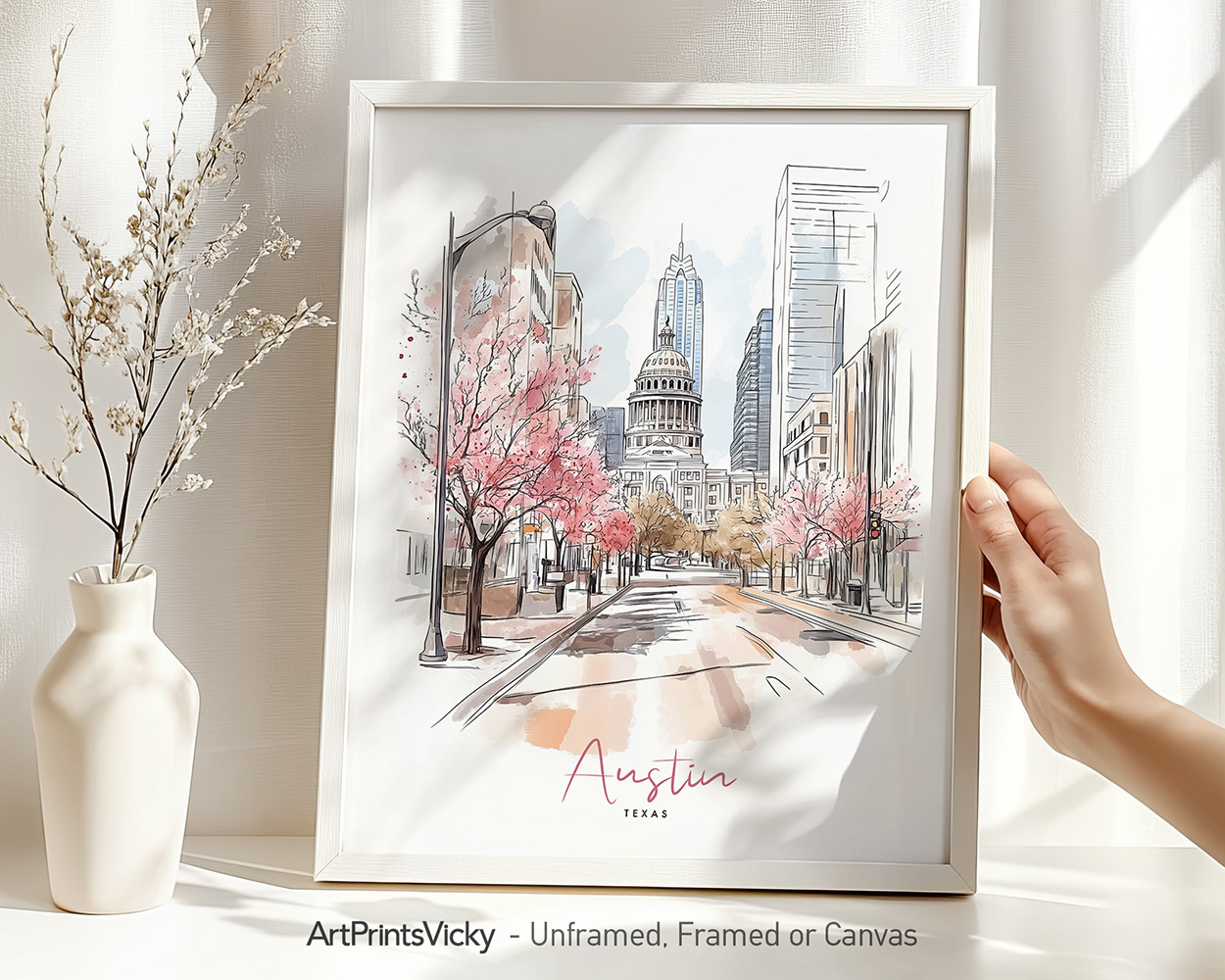 Hand holding a framed art print of Austin in watercolor drawing with soft pastel tones.