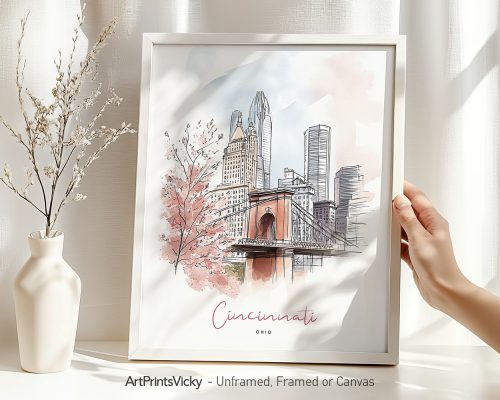 Hand holding a framed art print of Cincinnati in watercolor drawing with soft pastel tones.