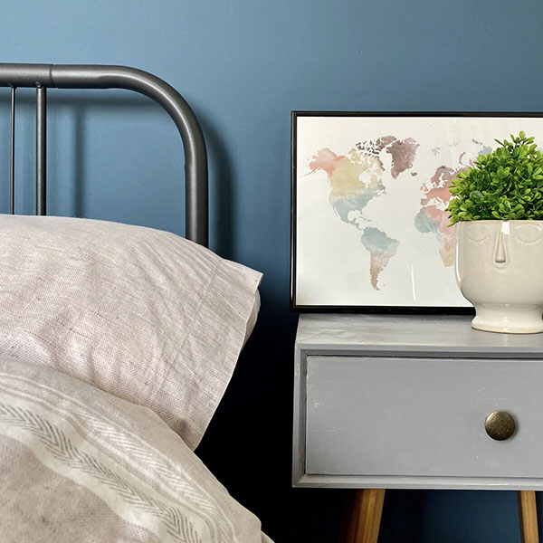 Framed world map print on a bedside table next to a plant in a white pot.