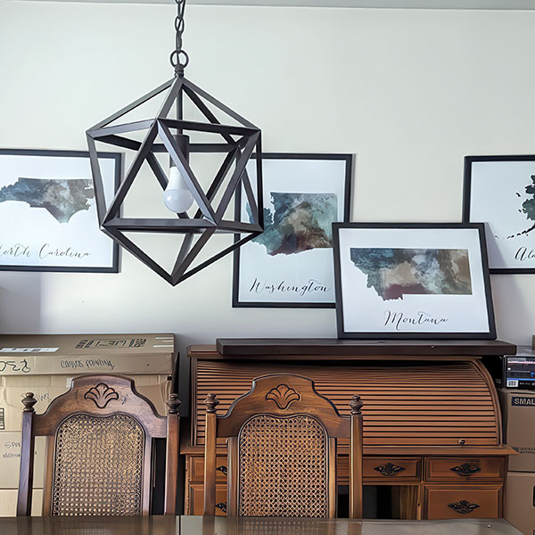 Geometric pendant light fixture hanging above wooden chairs and framed artwork on a wall.