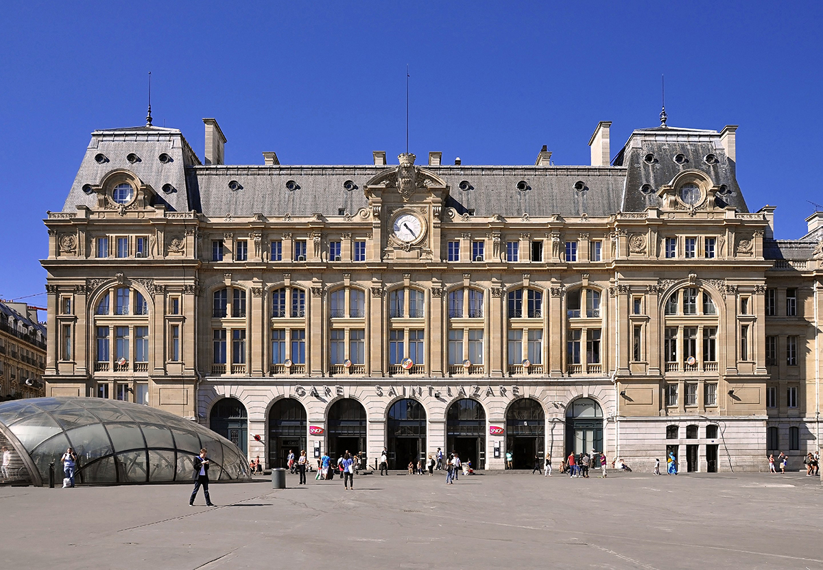 Facade of Gare de Paris Saint-Lazare with clock and arched windows under a clear blue sky.