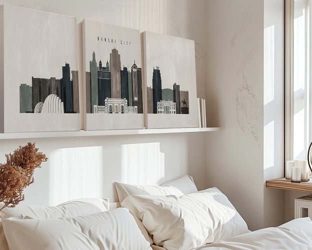 Three canvas prints depicting the Kansas City skyline in muted colors on a wall above a bed.