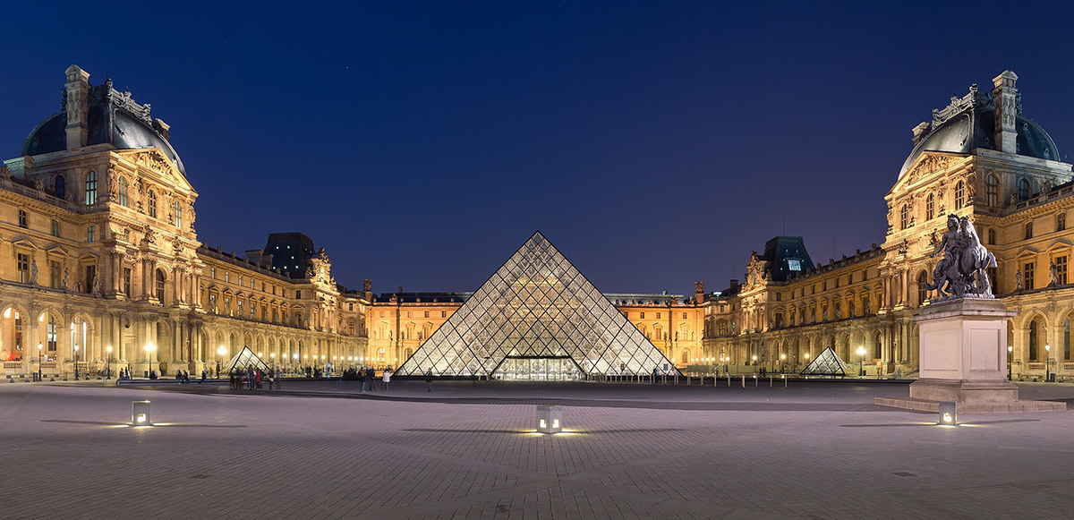 The Louvre Museum featuring the glass pyramid and surrounding architecture illuminated at night.