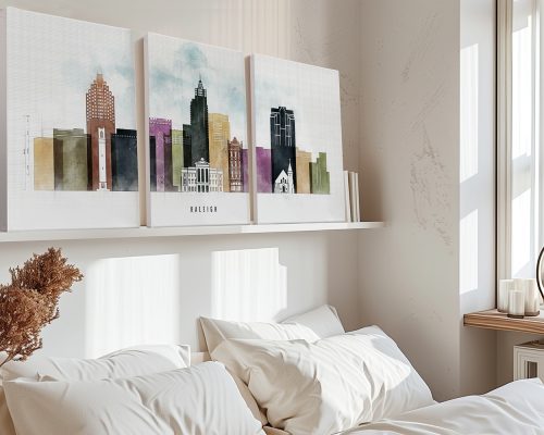 Three framed art prints of Raleigh's skyline displayed above a bed with white bedding.